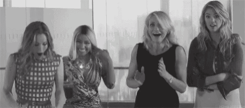 a group of women are standing next to each other in front of a window and smiling .