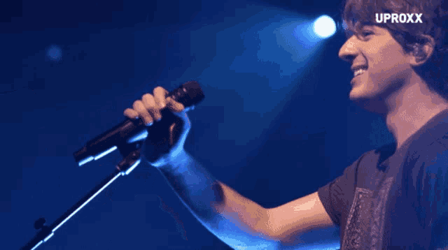 a man singing into a microphone with the word uproxx on the bottom right