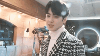 a young man wearing a suit and a turtleneck is standing in a room .