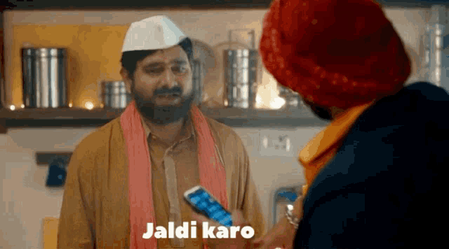 a man in a turban is talking to another man who is holding a cell phone and the words jaldi karo are on the screen