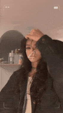 a woman holds her hand to her forehead in front of a cell phone that says rec
