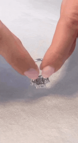a close up of a person 's hand holding a diamond ring .