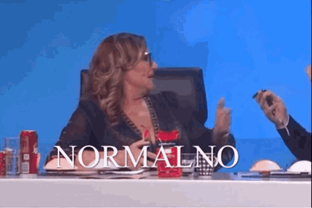 a woman is sitting at a table with the word normalno on the screen