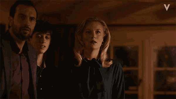 a man and two women are standing in a dark room with a white v in the corner