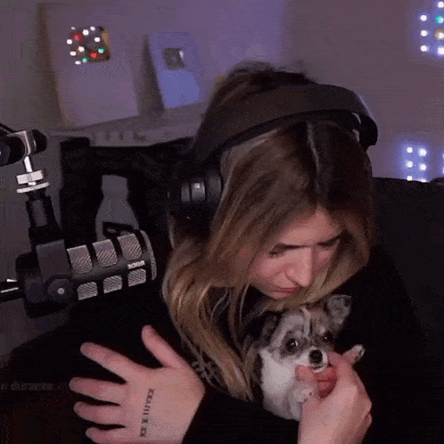 a woman wearing headphones holds a small dog in her arms with a tattoo on her arm that says xxi x xii