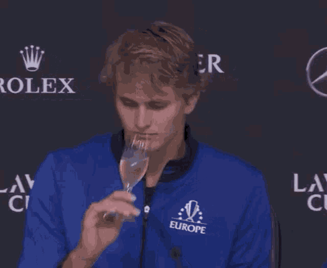 a man wearing a blue jacket is drinking from a glass .