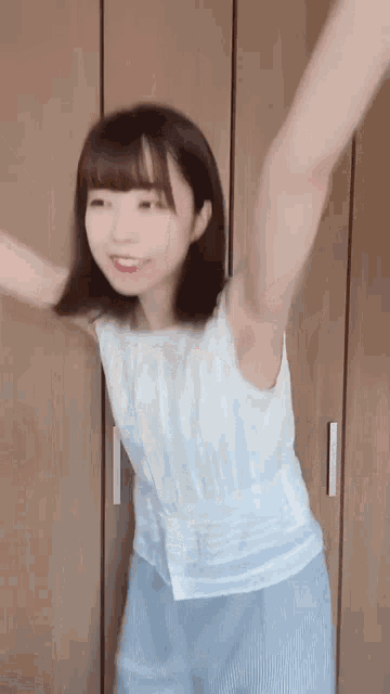 a young woman in a white tank top and blue shorts is dancing in front of a wooden wall .
