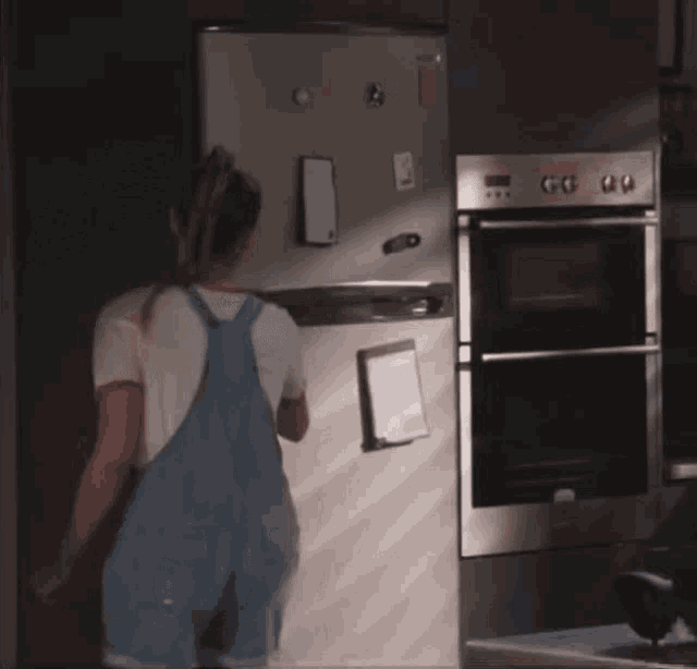 a woman in overalls stands in front of a refrigerator that has a sticker on it that says ' lg '