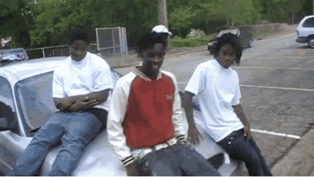 three young men are sitting on the hood of a car .