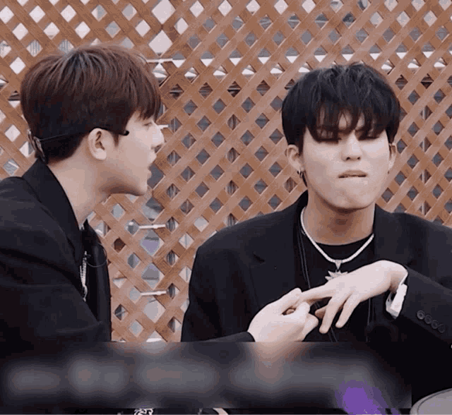 two young men are sitting in front of a wooden fence and one of them is making a face