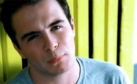 a man in a blue shirt is making a funny face while sitting in front of a yellow fence .