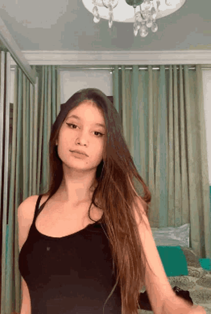 a woman in a black tank top is standing in front of a chandelier