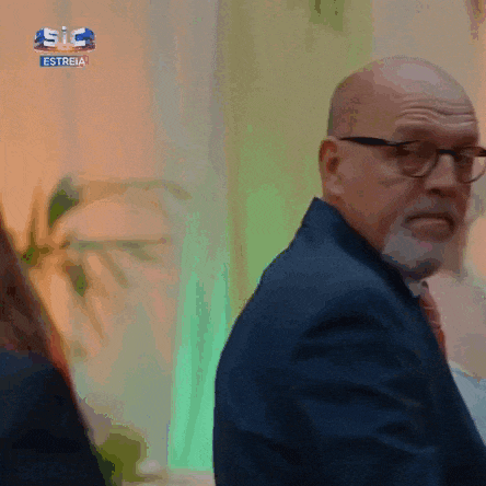 a man with glasses and a beard is standing in front of a sign that says estrela
