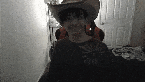 a man wearing a cowboy hat and a shirt with a sun on it smiles