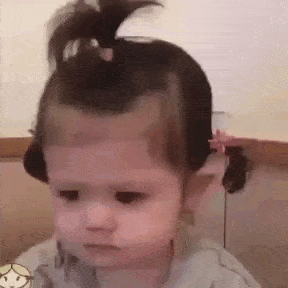 a little girl with a bun in her hair is making a funny face .