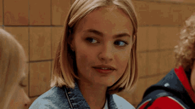 a young woman in a denim jacket is looking at the camera while sitting next to another young woman .