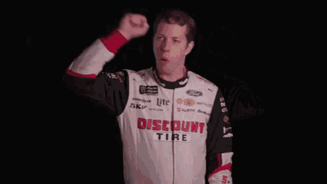 a man wearing a discount tire shirt holds his fist up in the air .