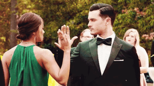 a man in a tuxedo and a woman in a green dress give each other a high five