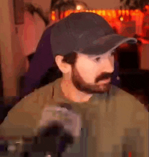 a man with a beard wearing a baseball cap is sitting in front of a computer .