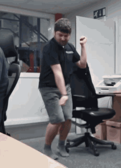 a man in a black shirt is dancing in front of an office chair