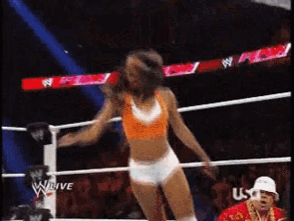 a woman is dancing in a wrestling ring while a man in a hat watches