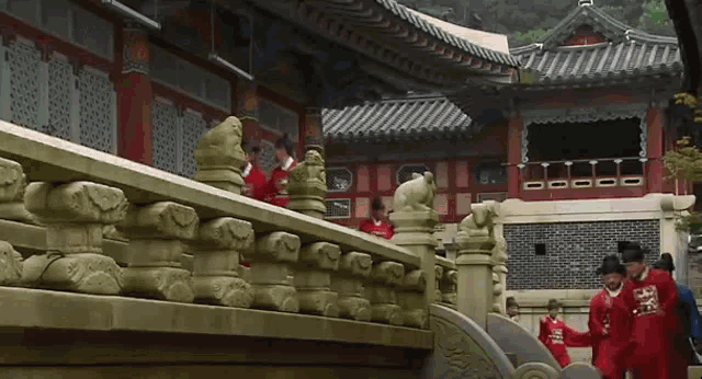 a group of men in red robes are standing on a bridge