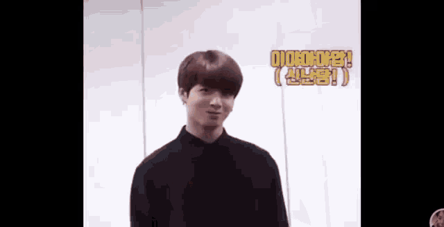 a young man in a black shirt is standing in front of a white wall and making a funny face .