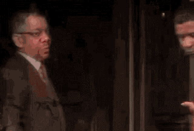 two men are standing next to each other in a dark room . one of the men is pointing at the other .