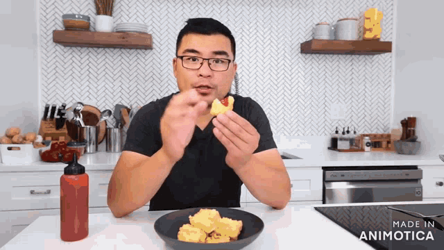 a man in a black shirt is holding a piece of food in front of a bowl of food and a bottle of ketchup