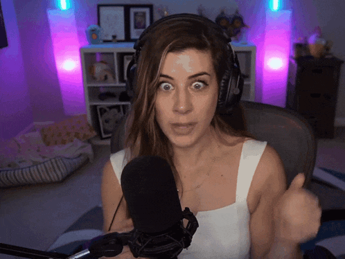 a woman wearing headphones stands in front of a microphone with a surprised look on her face