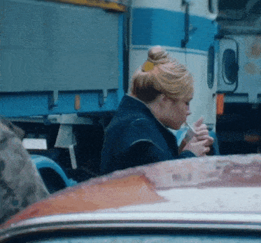 a woman is smoking a cigarette in front of a blue truck