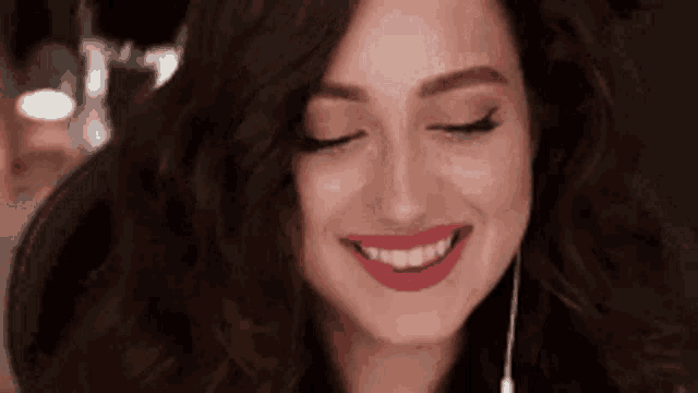a woman with red lipstick is smiling with her eyes closed while wearing headphones .