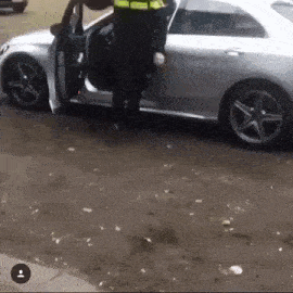 a police officer is standing next to a silver car in a parking lot .