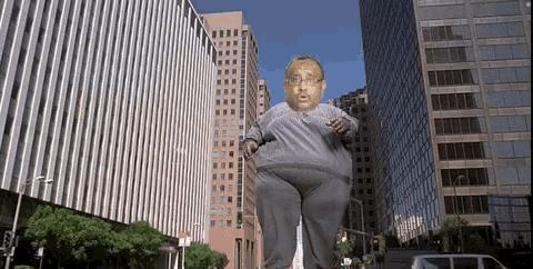 a giant man with glasses is walking down the street in front of tall buildings