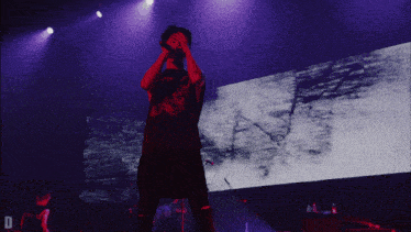 a man singing into a microphone on a stage with the letter d in the lower right corner