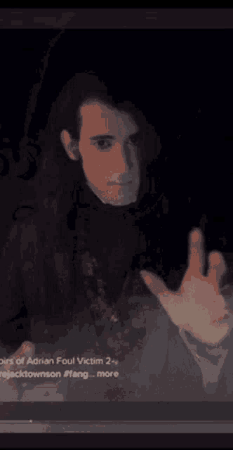 a man with long hair is reaching out his hand towards the camera .