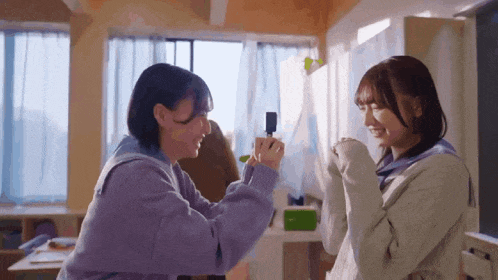 two girls are standing next to each other in a room and one is holding something in her hand .