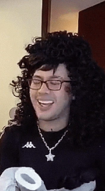a man wearing glasses and a kappa sweater smiles while holding a roll of toilet paper
