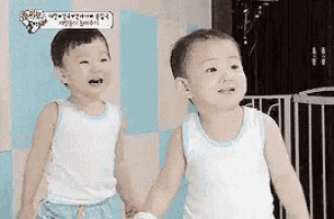 two little boys are holding hands and smiling while standing next to each other in a room .
