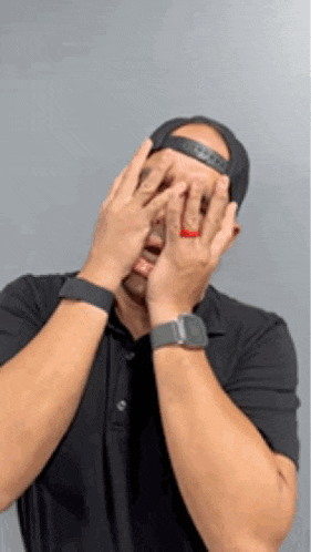 a man wearing a hat and a watch is covering his face with his hands