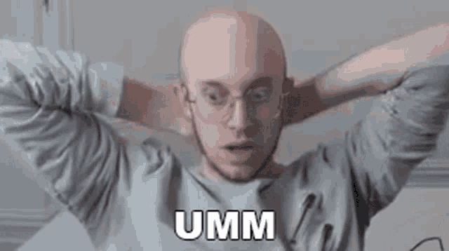 a bald man with glasses is sitting on a bed with his hands behind his head and says umm .