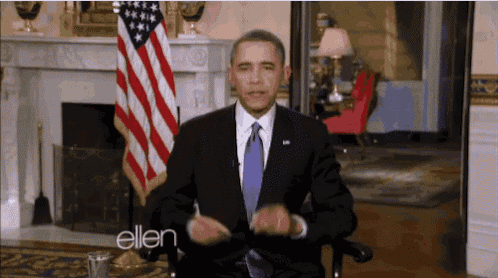 a man in a suit and tie is sitting in front of an american flag with the word ellen on the bottom right