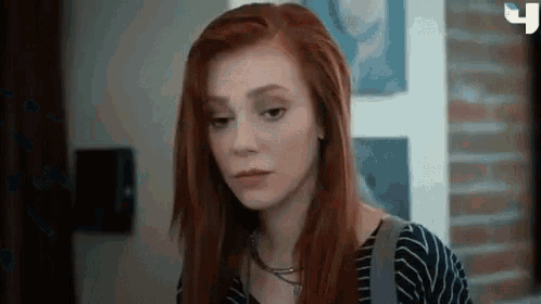 a woman with red hair is standing in front of a brick wall looking at the camera .