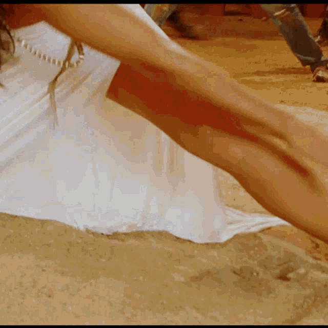 a woman in a white dress is laying in the sand with her legs crossed