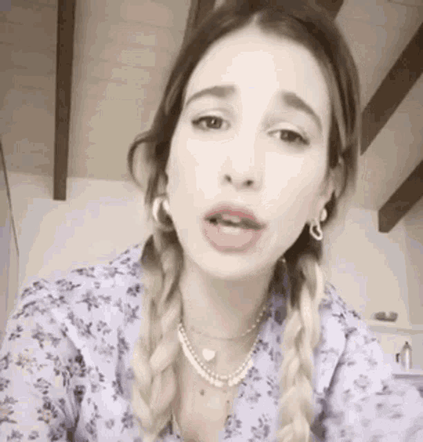 a woman wearing a purple floral shirt and a pearl necklace is making a funny face .