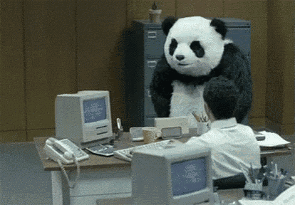 a man is sitting at a desk in front of a computer while a panda bear is standing next to him .