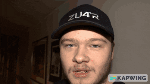a man wearing a black zu4r baseball cap looks at the camera