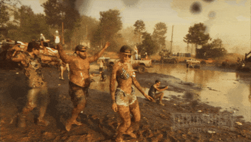 a woman in a bikini is dancing in the mud with a man in a hat