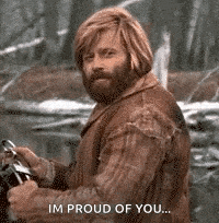 a man with long hair and a beard is holding a steering wheel and saying `` im proud of you '' .