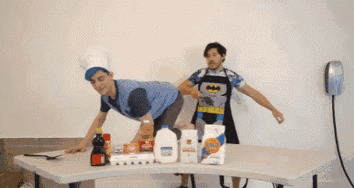 a man in a batman apron is standing next to a man in a chef 's hat